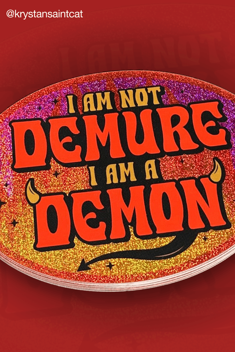 Ovale rood-gouden glittersticker met de tekst "I am not demure, I am a demon", duivelshoorns en staart