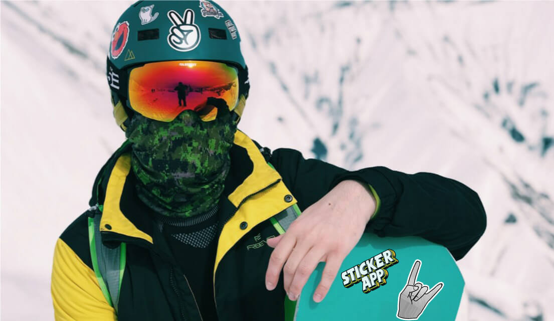 Snowboarder holding their snowboard with stickers on it and helmet.