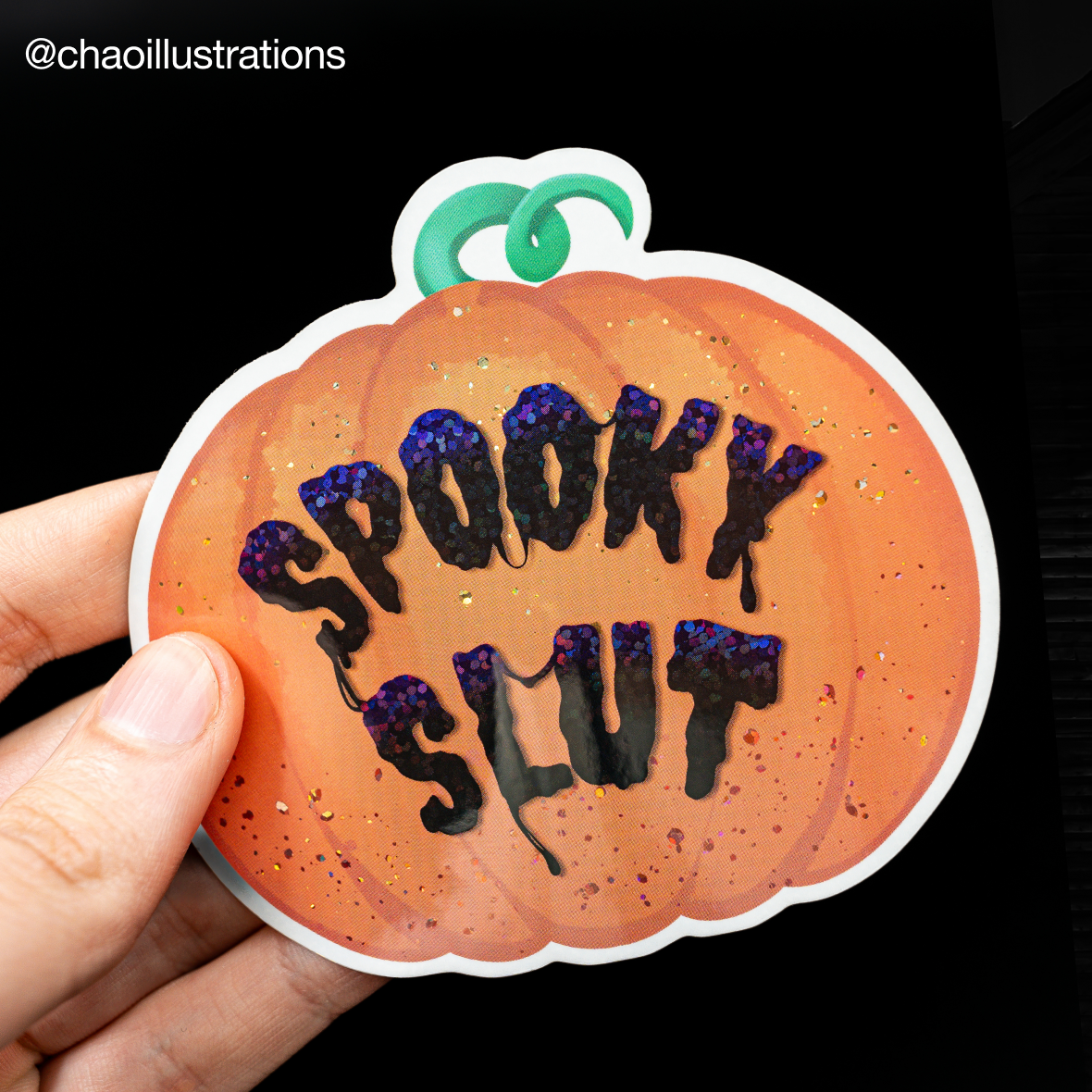 Hand met een contourgesneden pompoensticker met holografische glittertekst "Spooky slut"