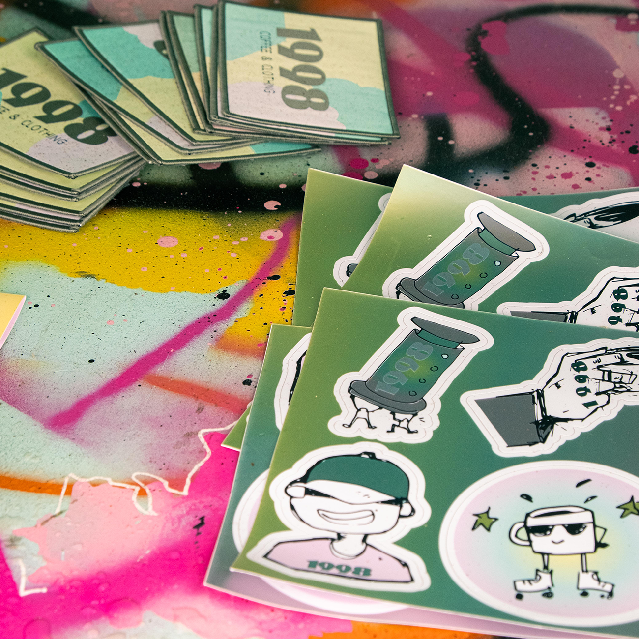 Sticker sheets and logo stickers with cartoon designs on a colorful, graffiti-splattered surface featuring numbers and characters.