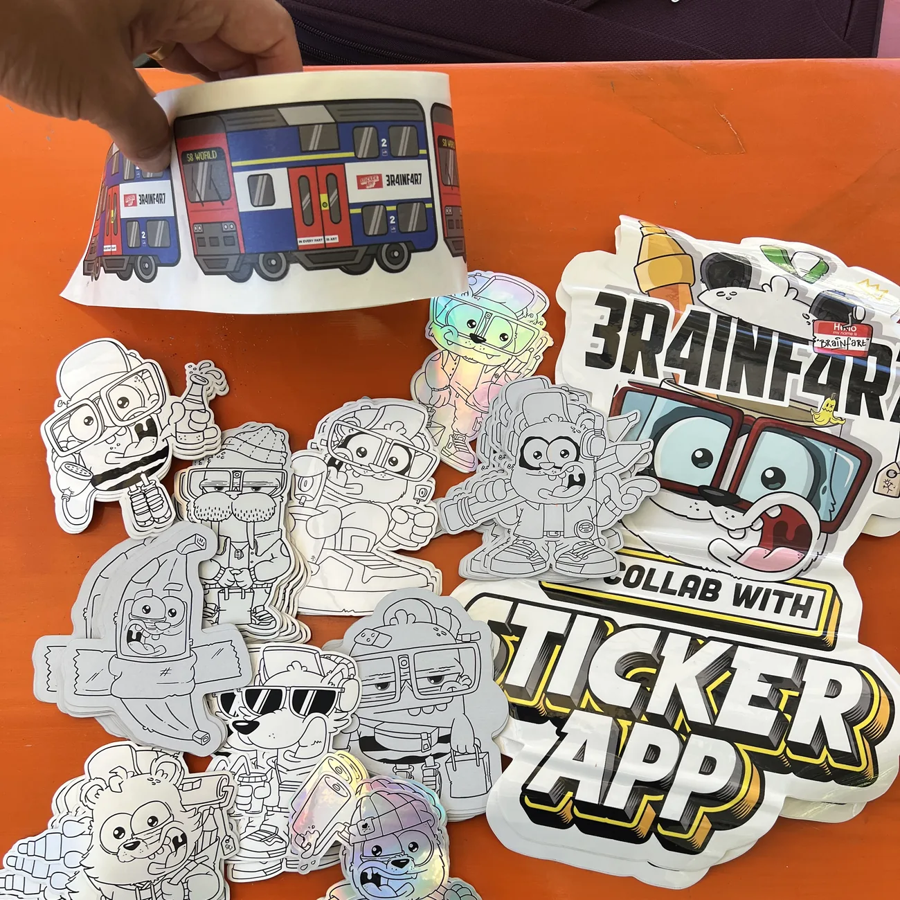 Etiket met de S8 World-trein van Brainfart x StickerApp met het bordje "In every fart is art", boven zwart-witte contourgesneden stickers gehouden