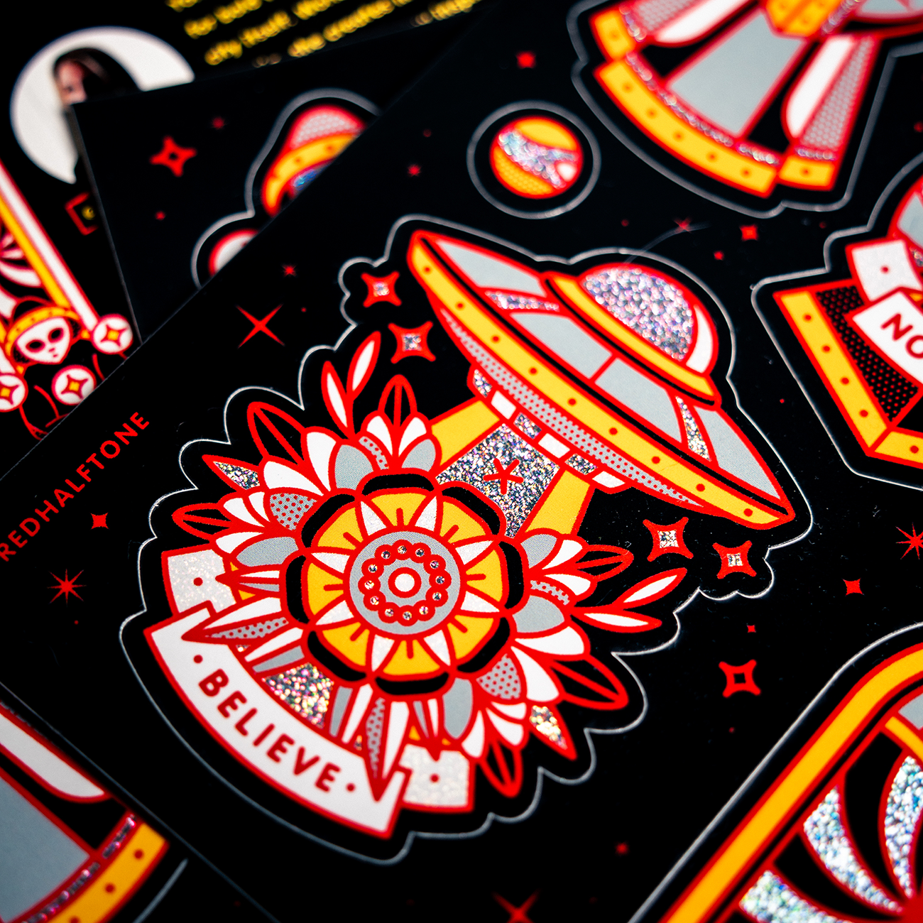 Colorful pixie dust stickers featuring UFOs, flowers, and the word "Believe" on a dark background with red and yellow accents.