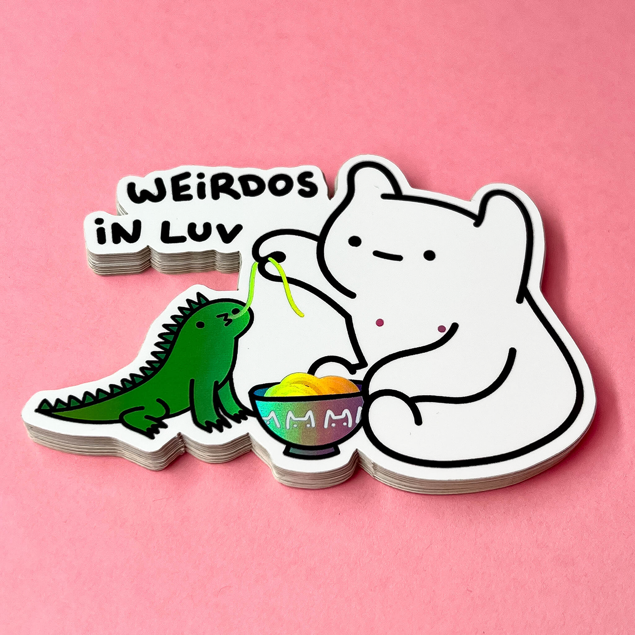 Illustration of a white bear and green iguana sharing noodles from a bowl with the text "WEIRDOS IN LUV" on a pink background.