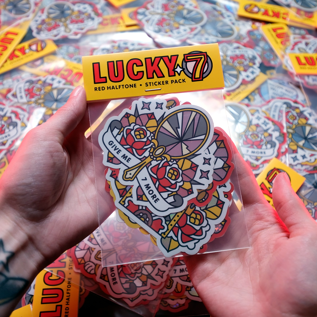 Hands holding a colorful sticker pack labeled "Lucky 7," featuring holographic, glitter and mirror stickers.