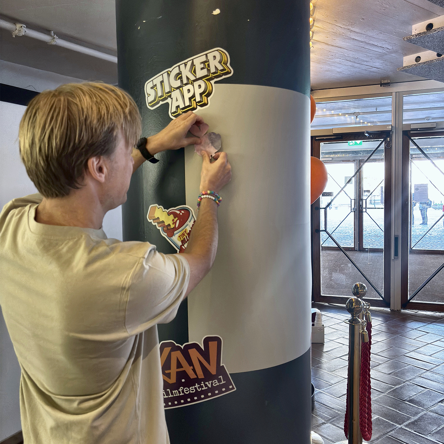 Man plakt een sticker op een StickerApp-stickermuur rond een pilaar op het KAN Film Festival