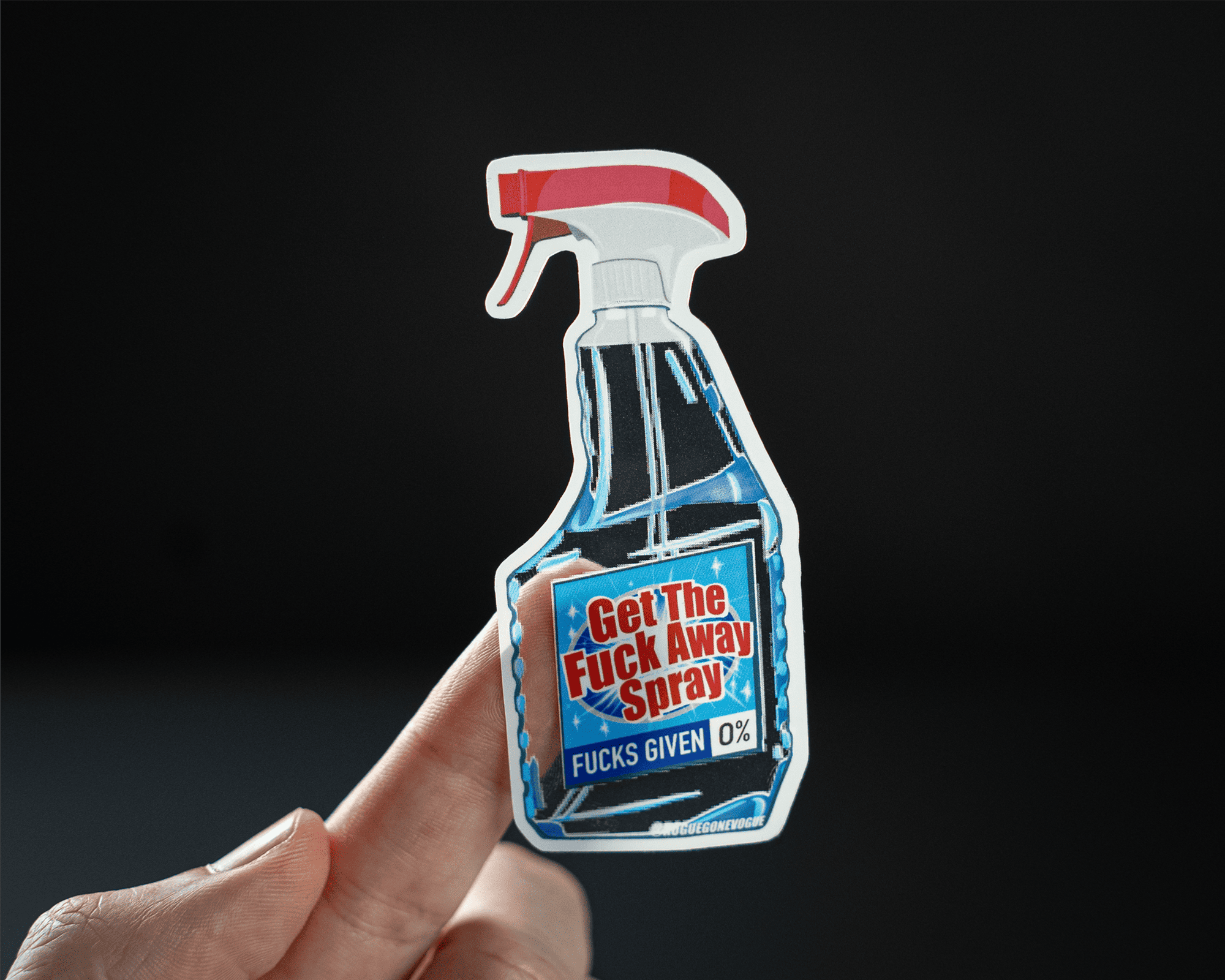A hand holds a transparent sticker shaped like a spray bottle labeled "Get The Fuck Away Spray" with "Fucks Given 0%" on a dark background.