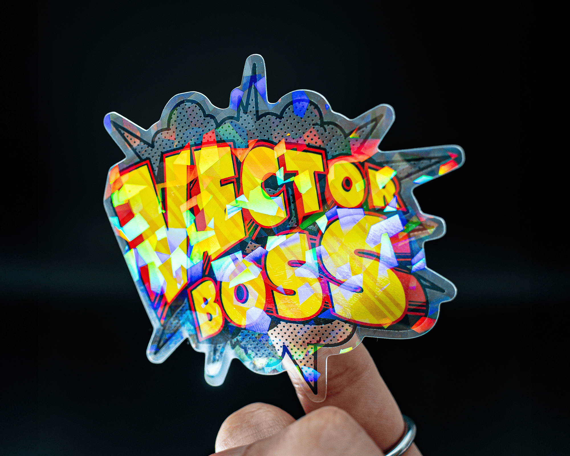 Colorful cracked ice sticker with "VECTOR BOSS" in bold, graffiti-style letters on a jagged, vibrant background, held between fingers.
