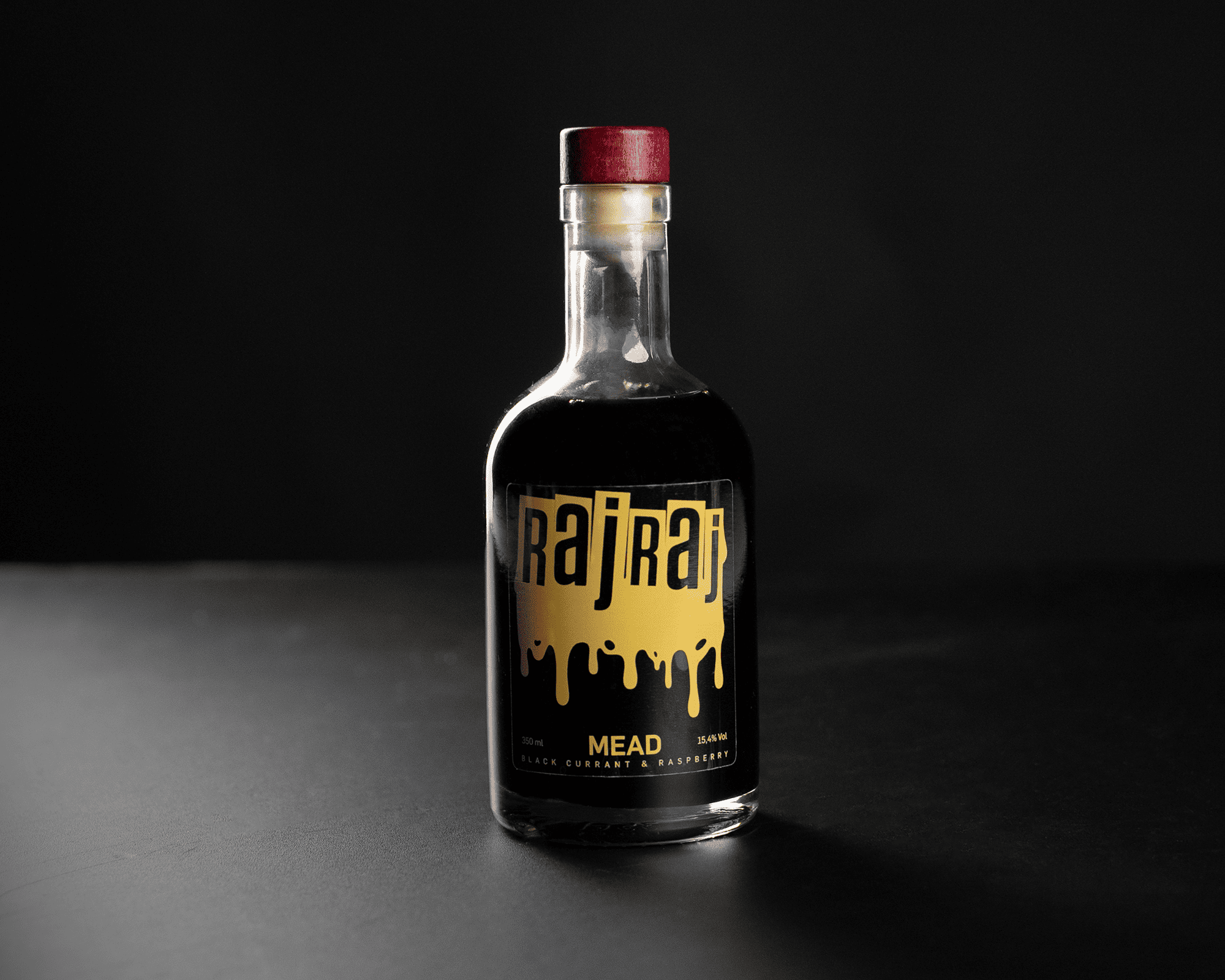 A bottle of dark mead with a red cap, with transparent label "RajRaj" and "Black Currant & Raspberry," against a black background.