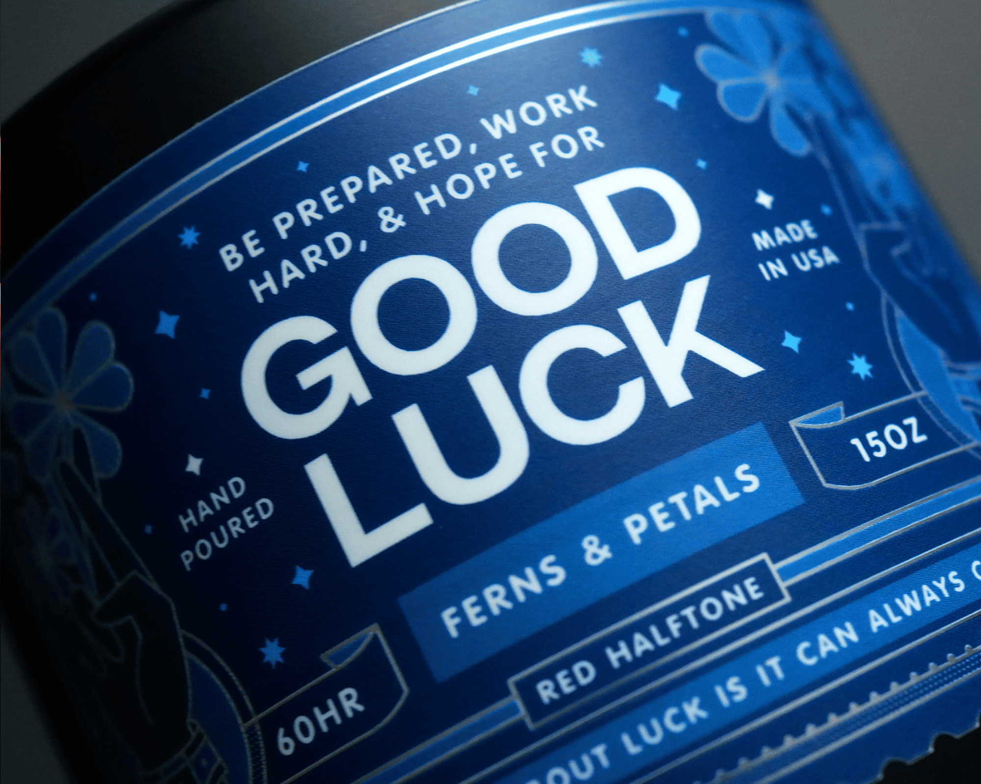 Close-up of a blue candle label reading "GOOD LUCK" with decorative elements and text about preparation and hope. Made in USA, 15oz.