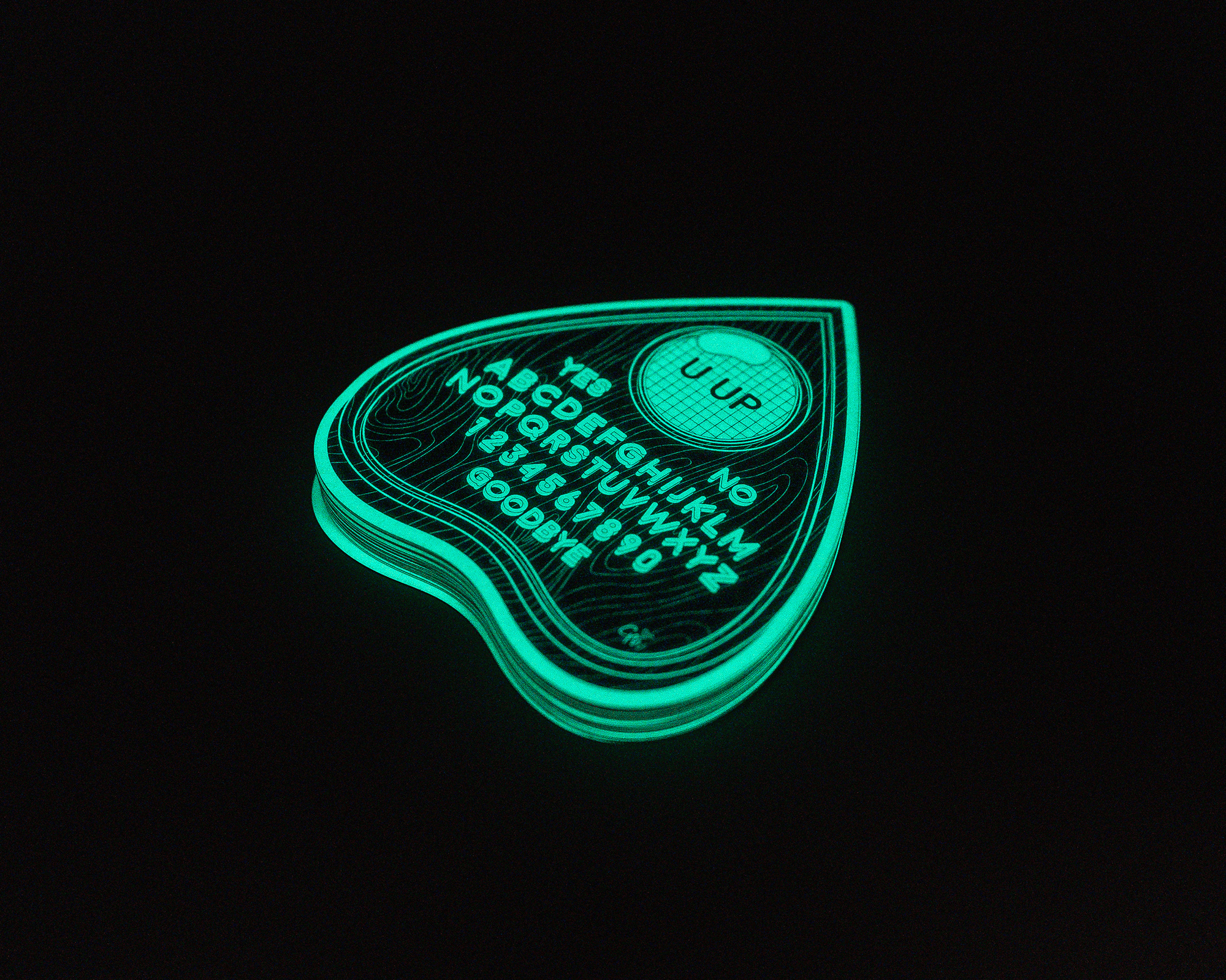 Glowing sticker planchette with alphabet, numbers, "YES," "NO," and "GOODBYE" options, used for a spirit board, on a black background.