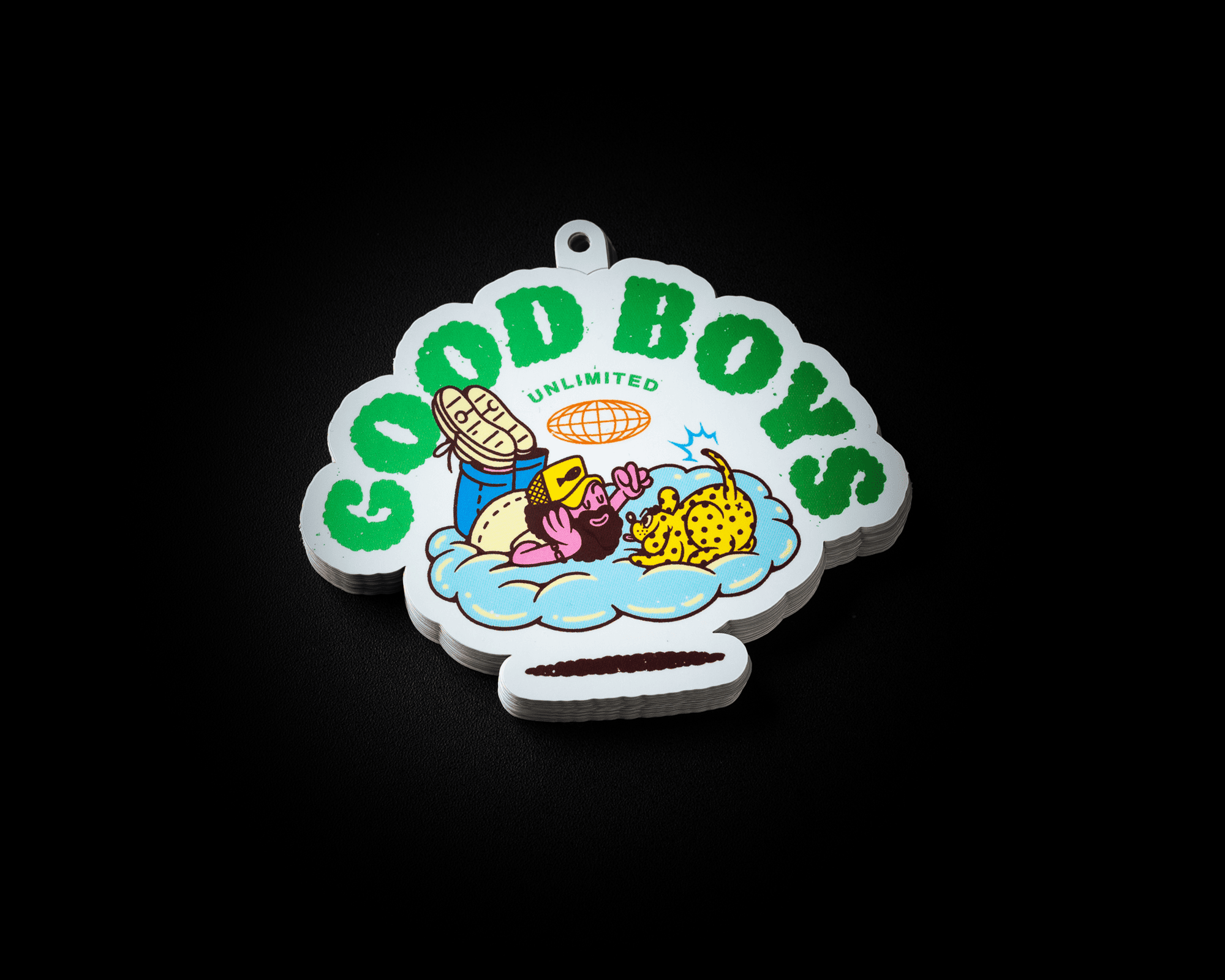A colorful cartoon hang tag with "Good Boys Unlimited" text, featuring a cowboy and a leopard relaxing on a cloud against a black background.