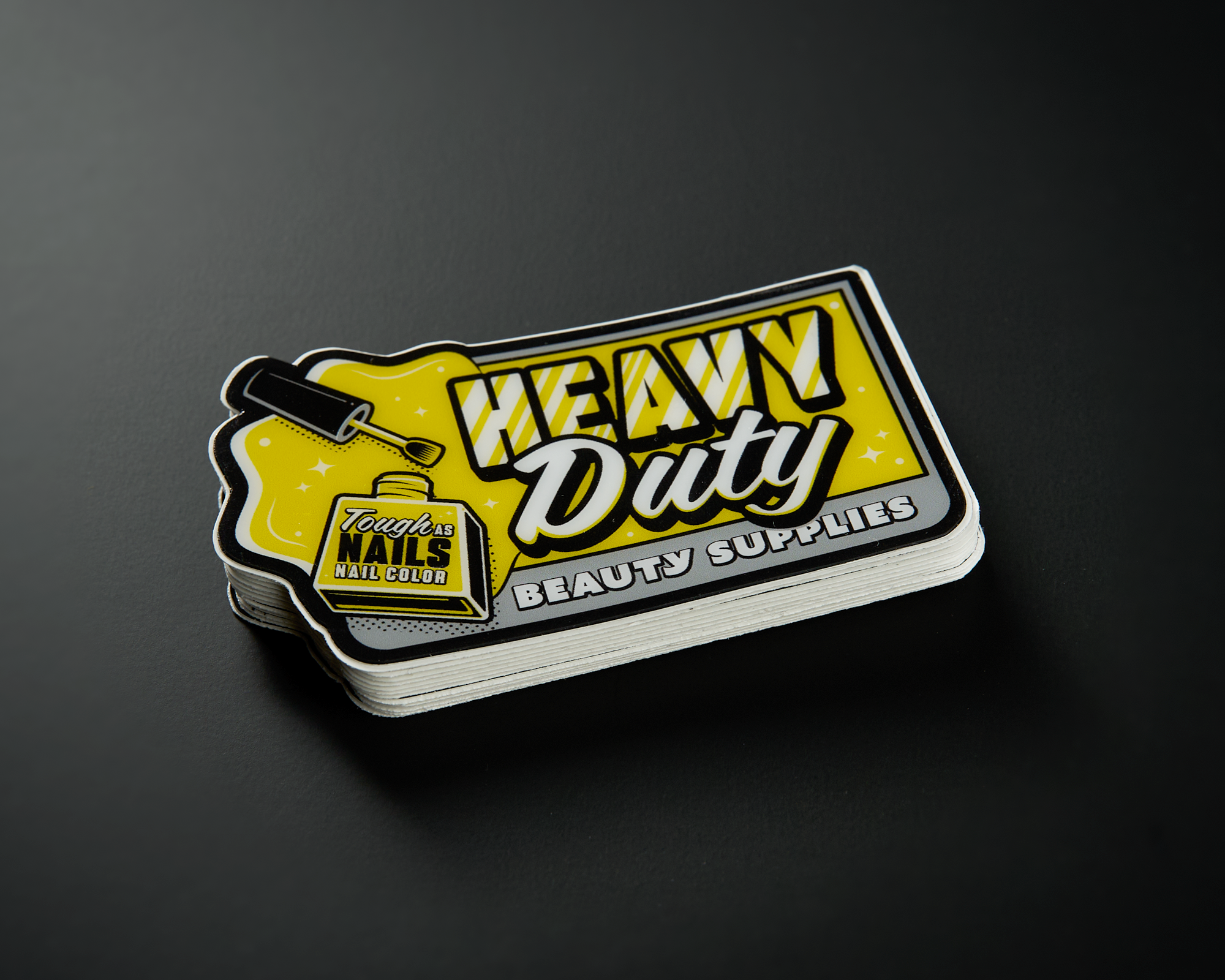 Stack of "Heavy Duty Beauty Supplies" stickers with yellow and black design, featuring a nail polish graphic.