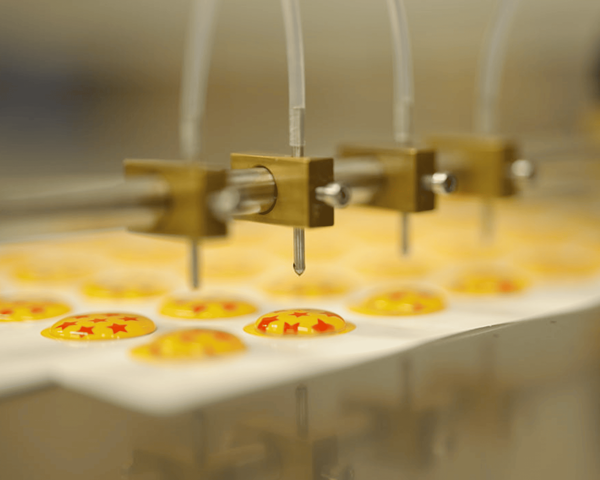 Close-up of a epoxy machine creating small, round objects with red stars on a yellow background.