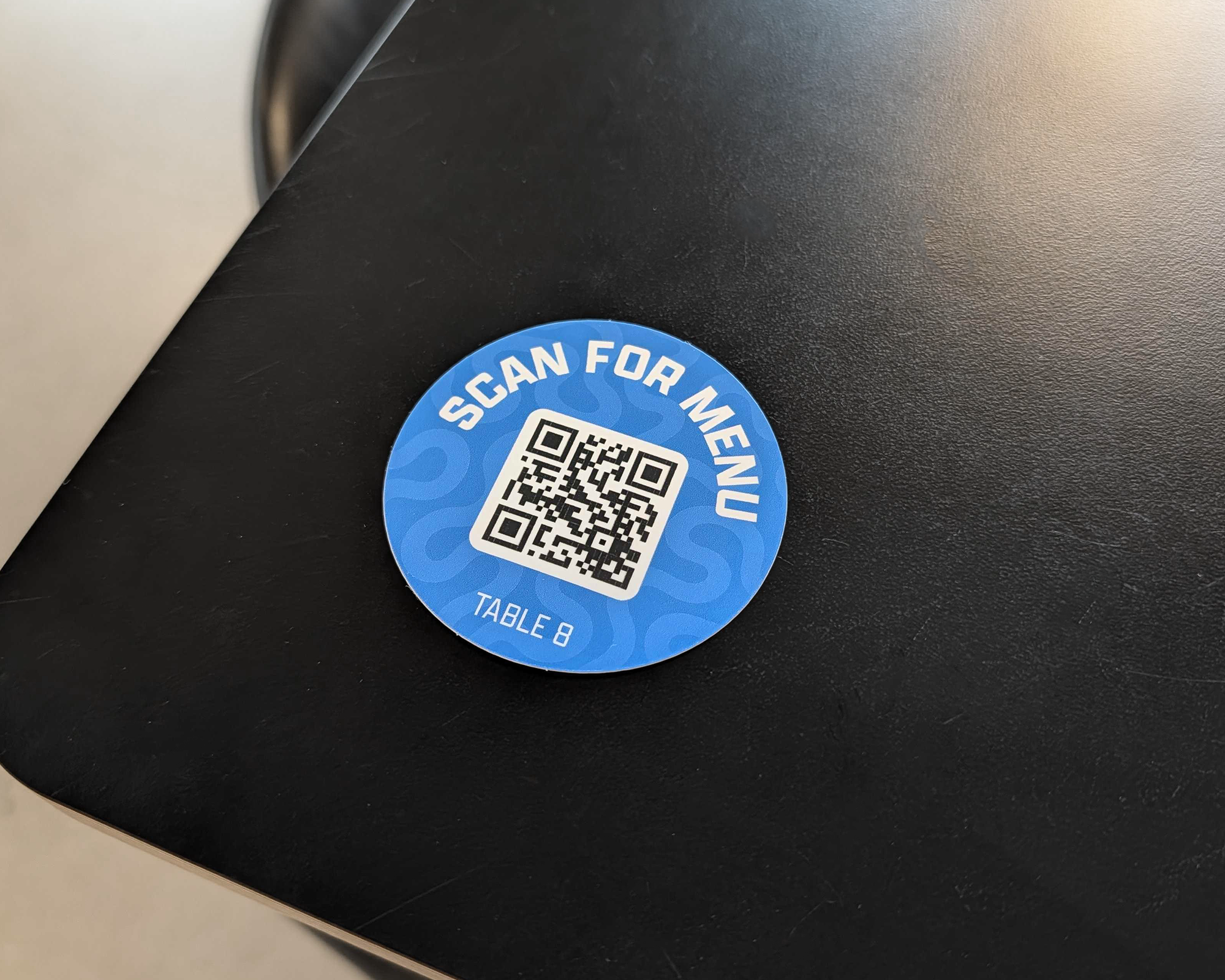Blauwe QR-codesticker "Scan for menu" voor tafel 8 op een zwarte tafel