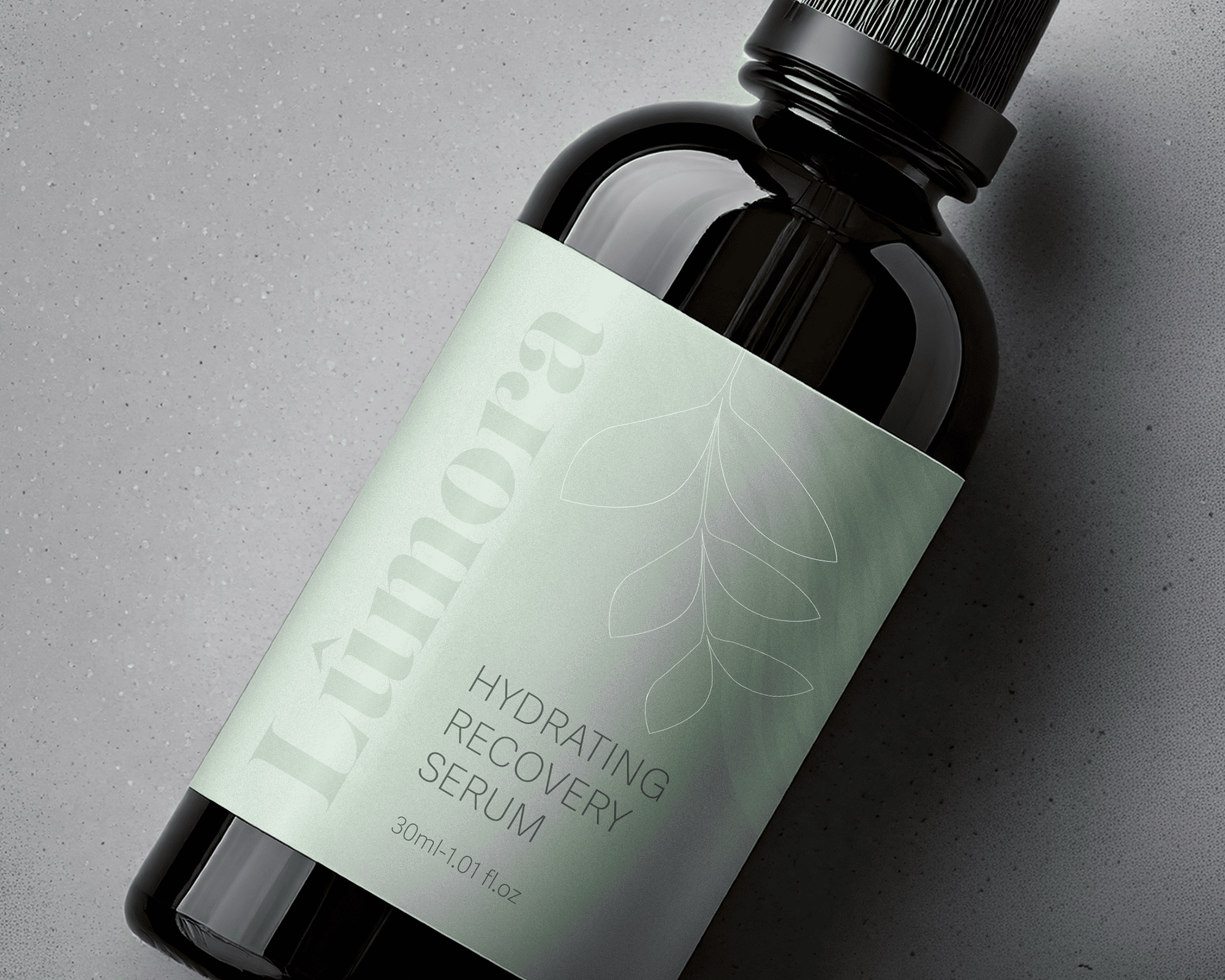 A dark bottle labeled "Lùmora Hydrating Recovery Serum" with a green leaf design, placed on a speckled gray surface.