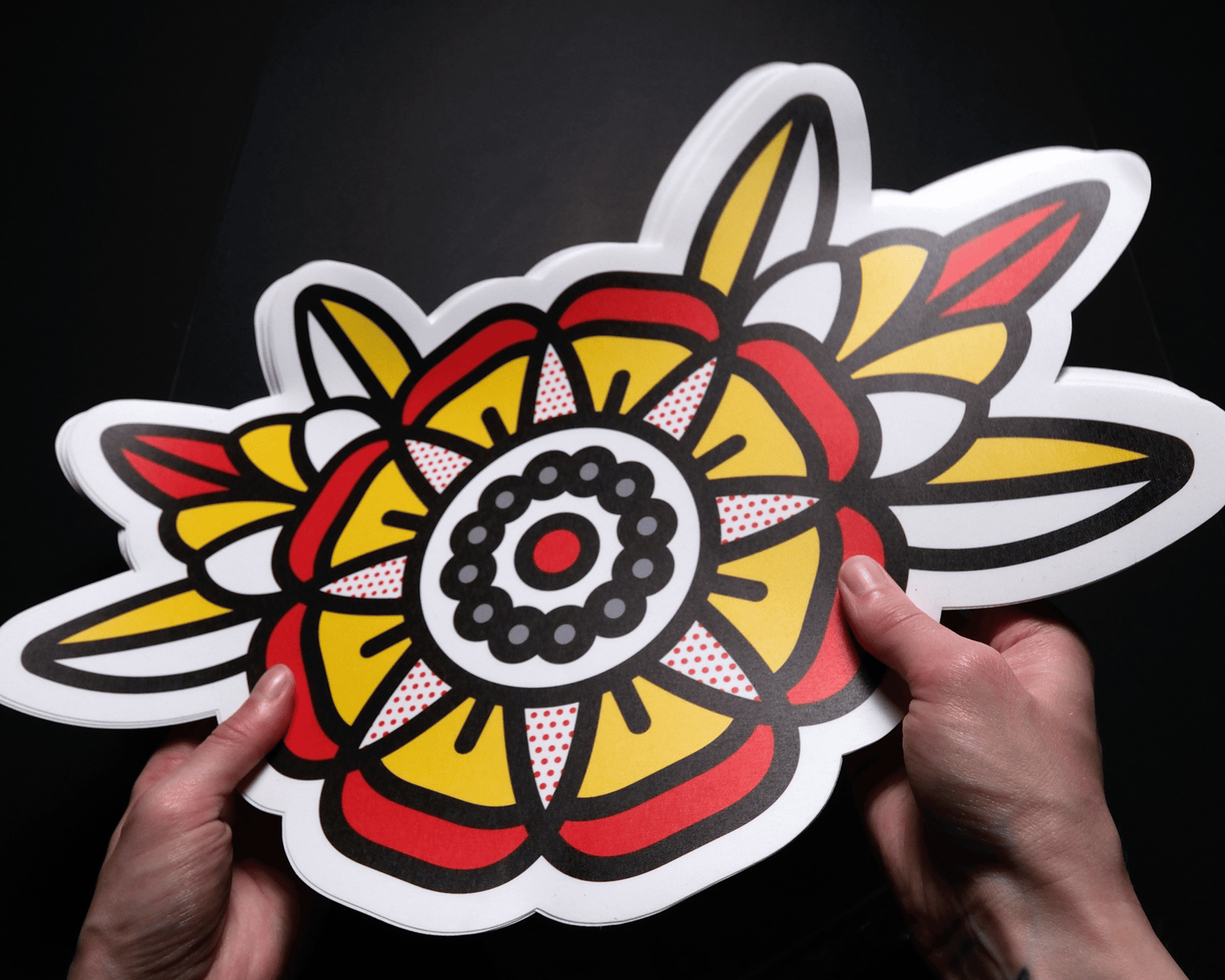 Hands holding a vibrant, large wall sticker with a bold, abstract floral design in red, yellow, and black on a dark background.