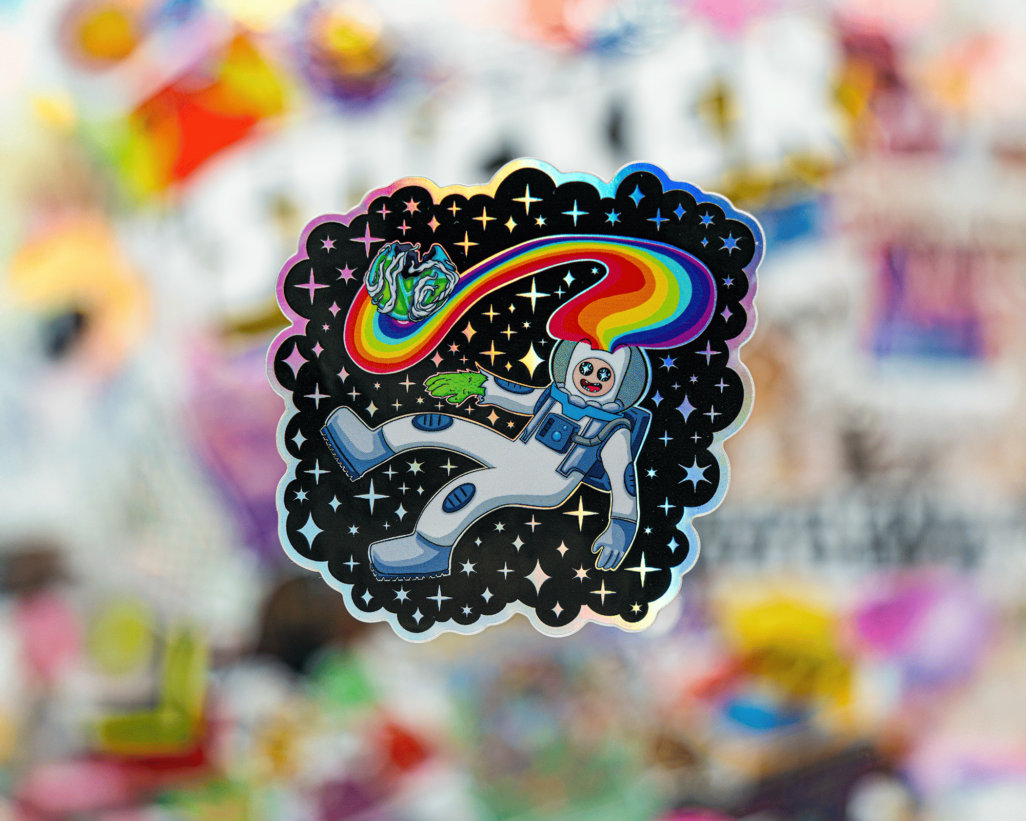 Holographic sticker of an astronaut floating in space. A rainbow trails from the astronaut's helmet against a starry background.