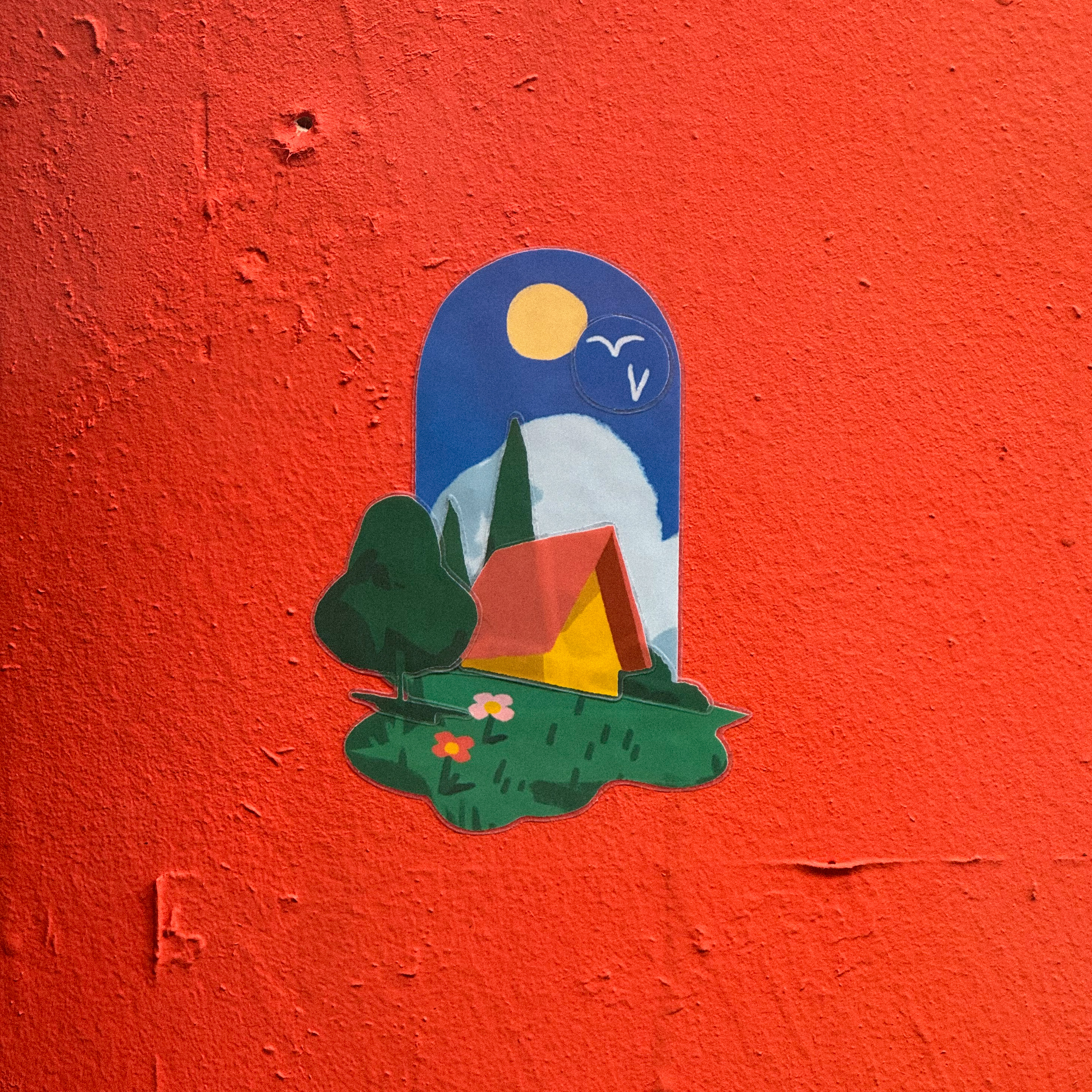 Colorful sticker of a house, trees, and moon on a bright red textured wall.