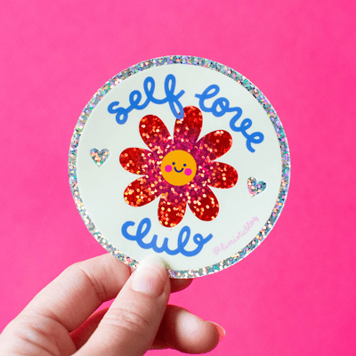 A round sparkly sticker of a flower with the text self love club.
