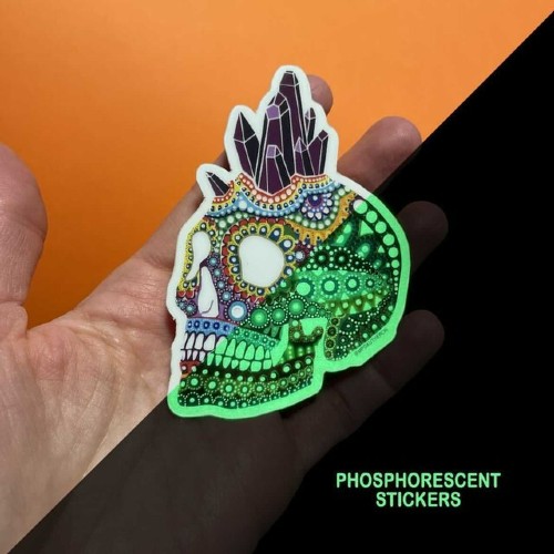 Hand met een mandala-doodskopsticker van mpgautheron, half zichtbaar groen oplichtend in het donker
