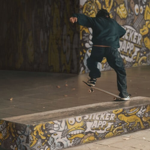 A skateboarder performs a trick on a graffiti-covered ledge, surrounded by vibrant street art.