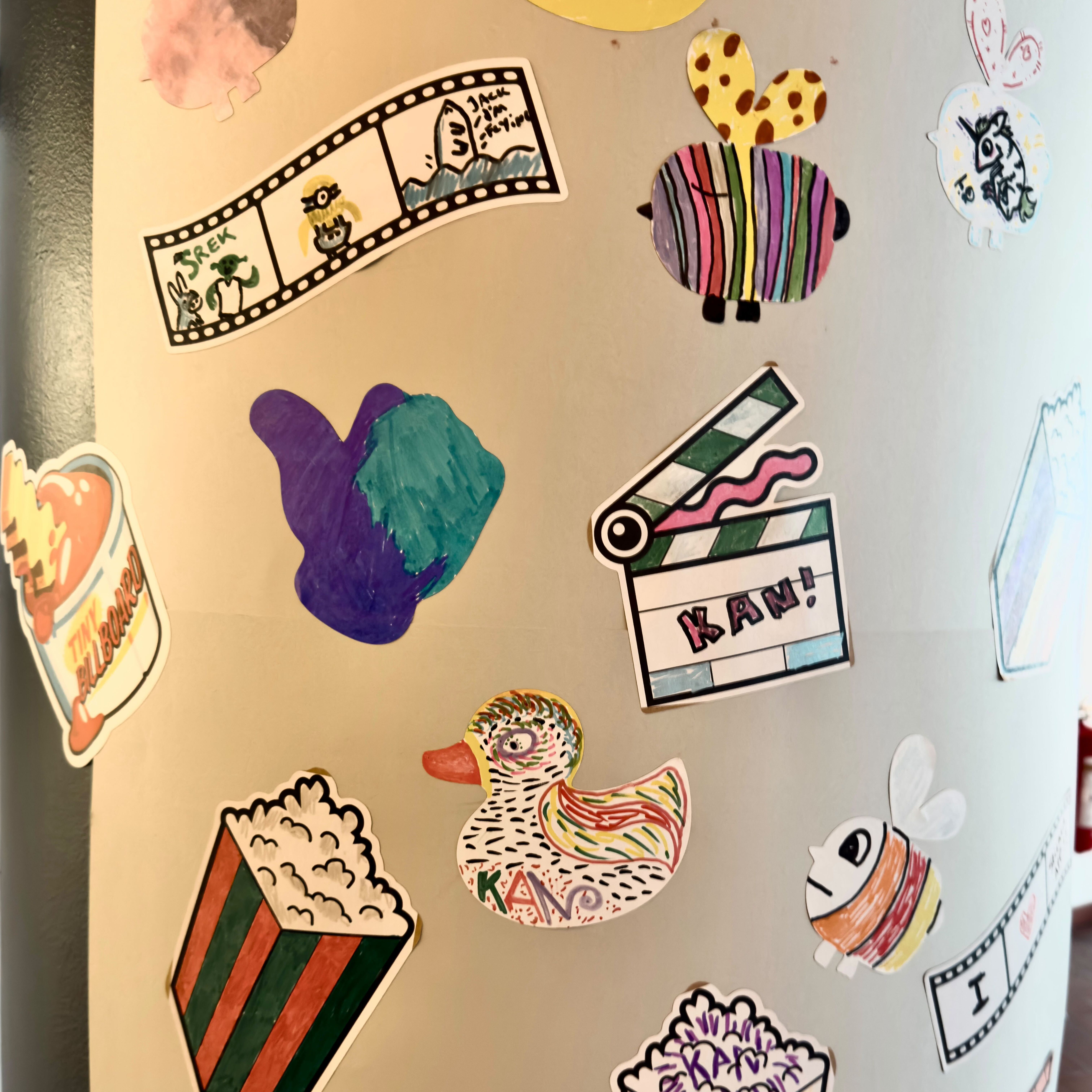 Pilaar vol handgetekende stickers van bezoekers van het KAN Film Festival, met onder meer popcorn, filmstroken, een eend en een klapbord met de tekst “KAN!”