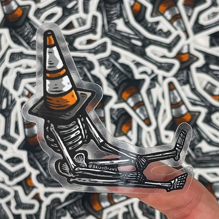 Transparante contourgesneden sticker van een skelet dat op de grond zit met een verkeerskegel op zijn hoofd, tegen een achtergrond van stickers.