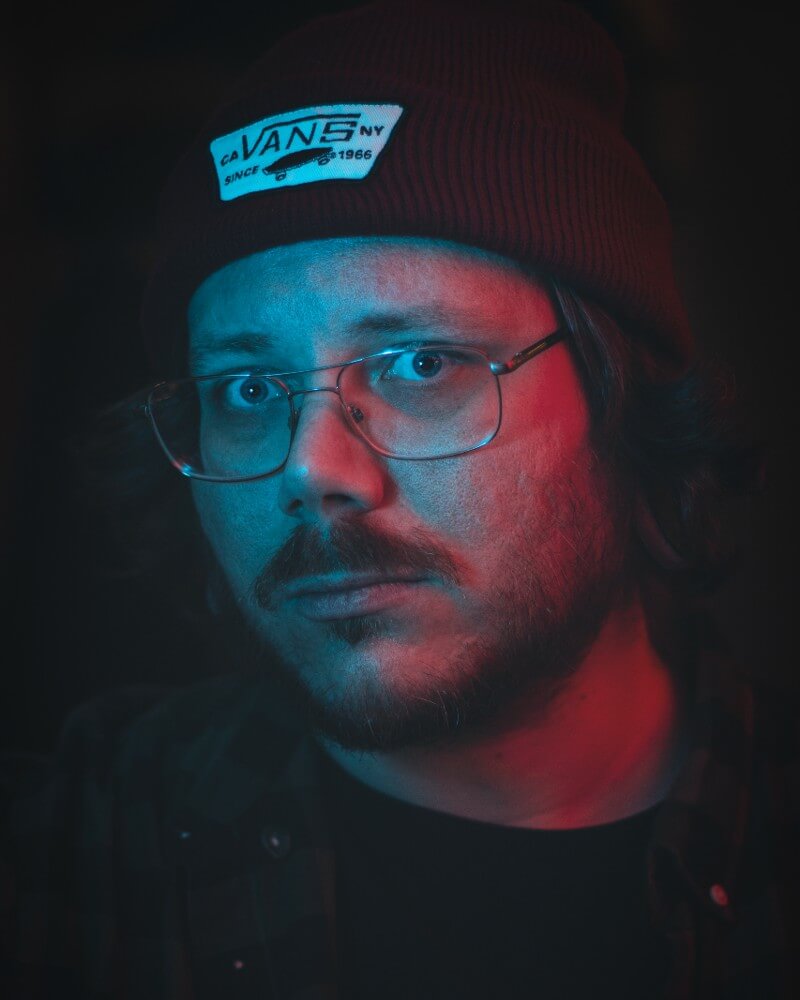 Portret van kunstenaar Emil Ronnelin (Bloodstrokes) met bril en muts in rood en blauw licht